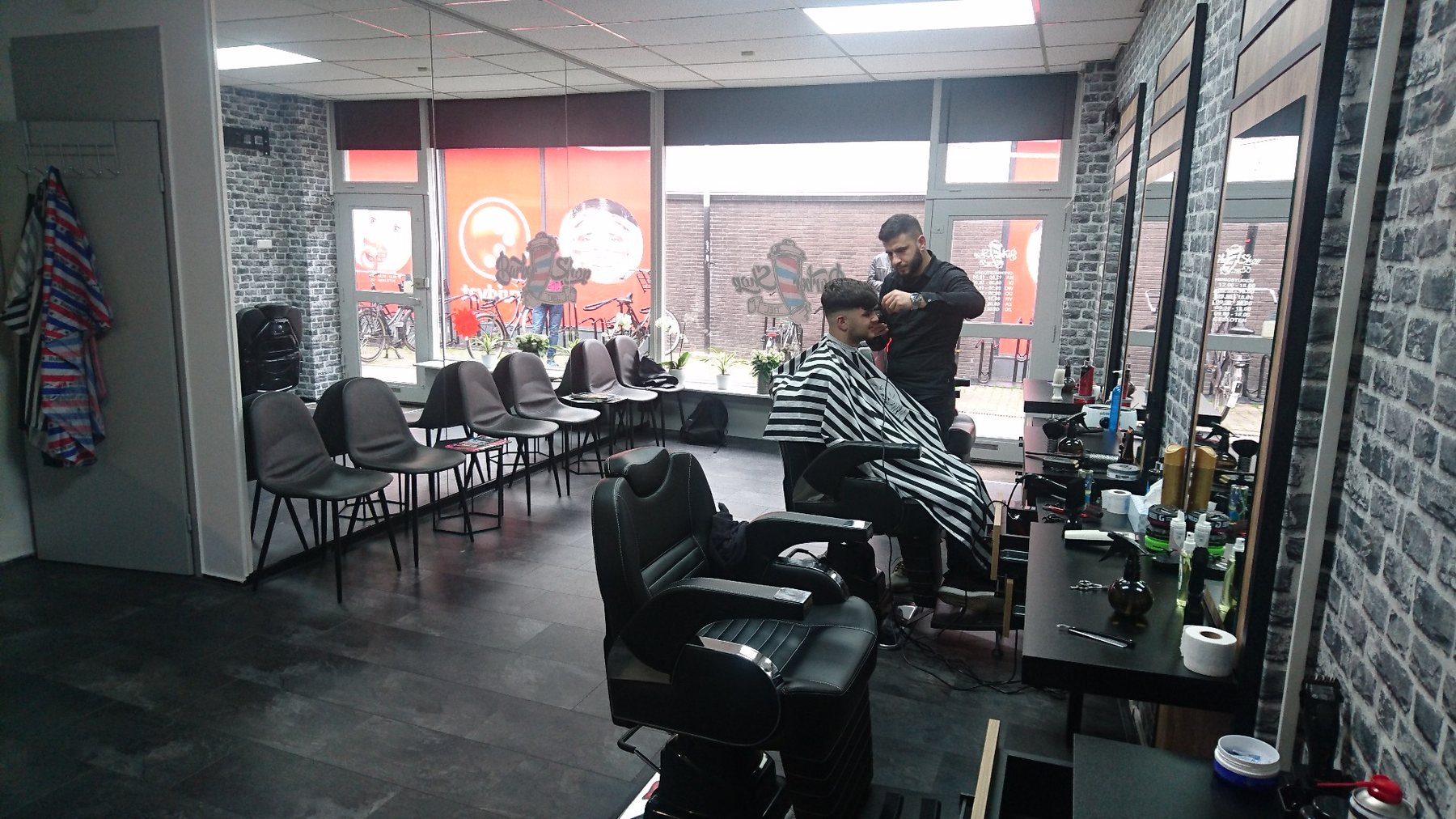 De zaak met wachtstoelen bij het raam en een barbier aan het werk