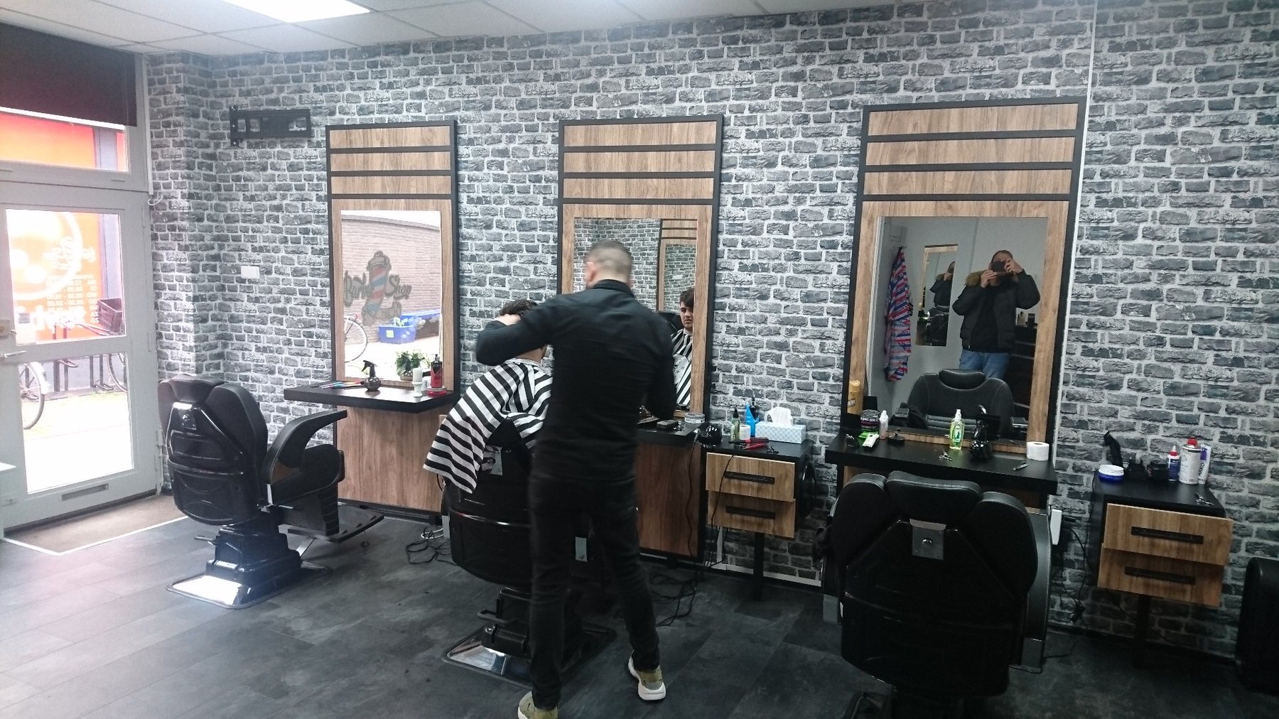 Drie werkplekken met spiegels en een barbier aan het werk